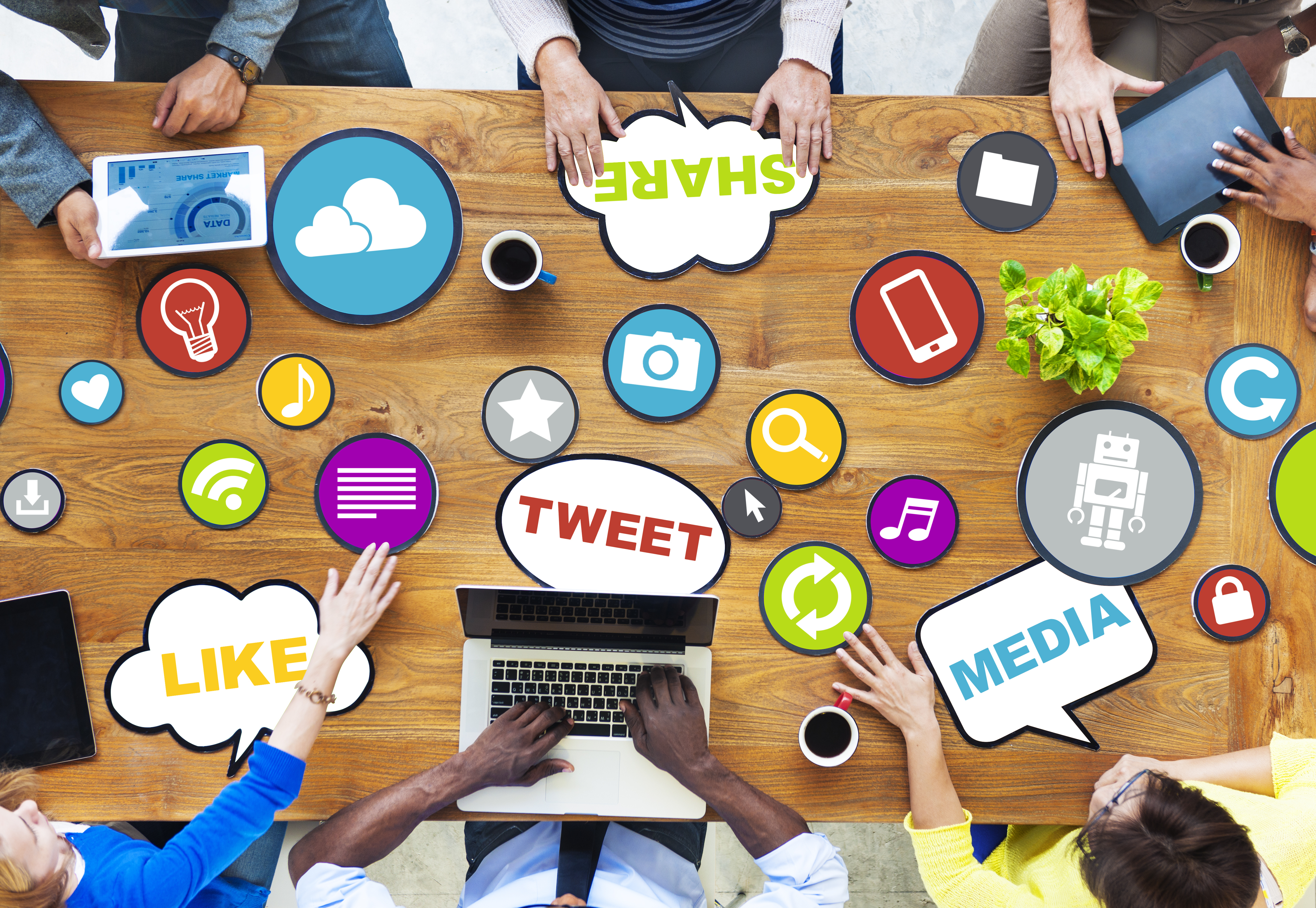 a group of people meeting at a conference table with tablets and laptops with speech bubbles indicating they are discussing social media ideas and strategies
